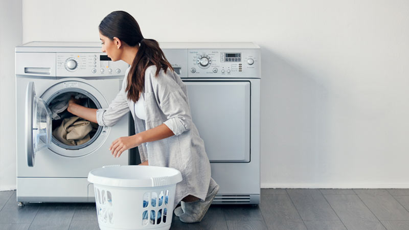 Mulher agachada coloca roupa na máquina de lavar roupa